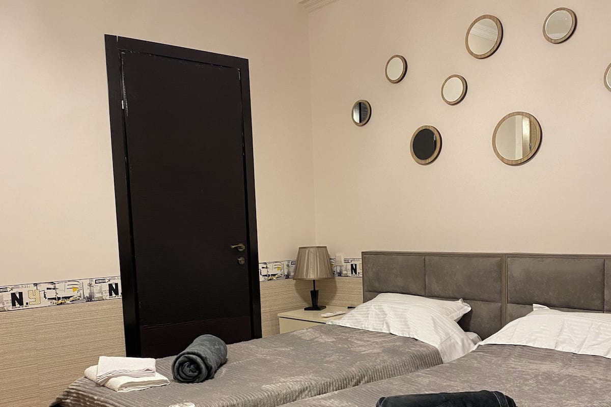 A hotel room with two beds, a nightstand, a lamp, and a door.