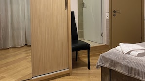 A room with a sliding wooden door, a black chair, a bed with a white blanket, and a tiled wall. - Siqvaruli (Tbilisi)