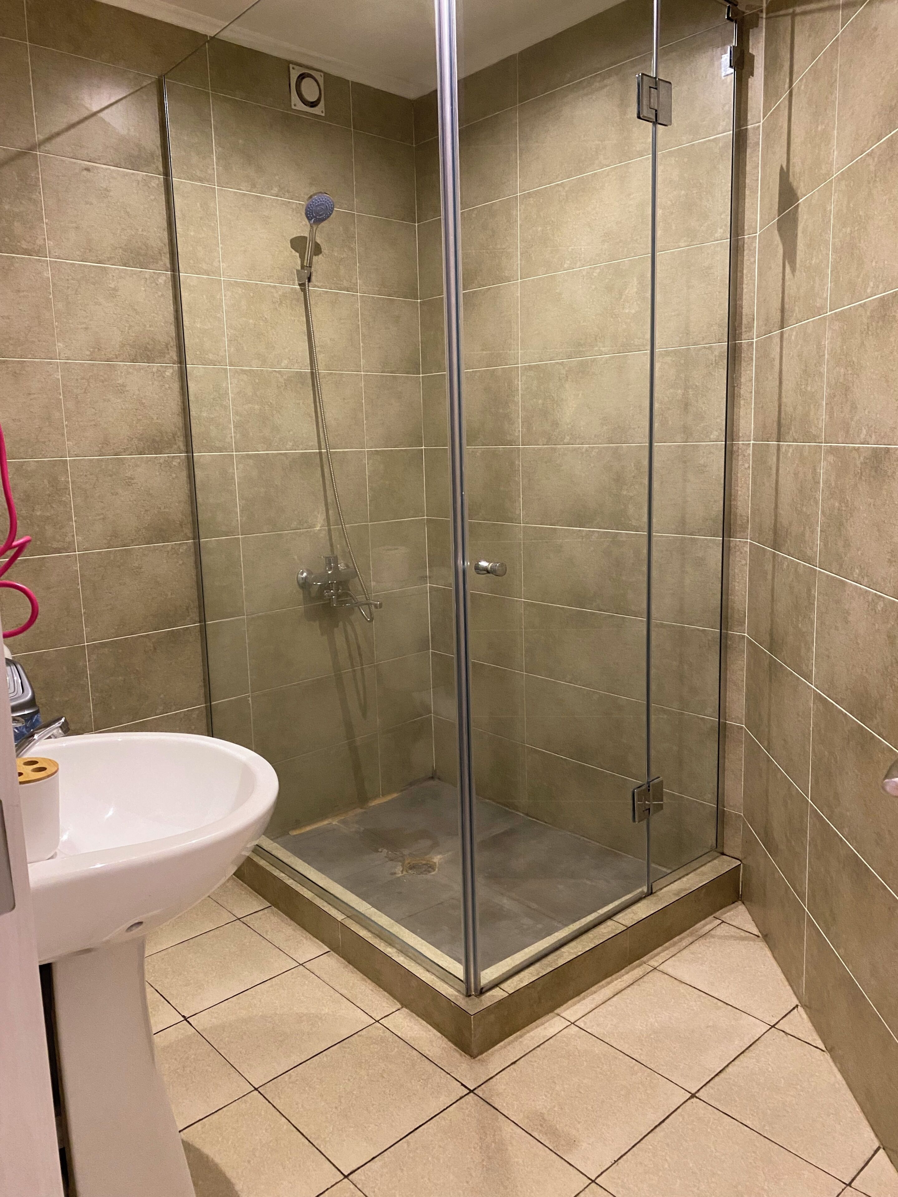 Ein Badezimmer mit einer Duschkabine, einem weißen Waschbecken und beige gefliesten Wänden.