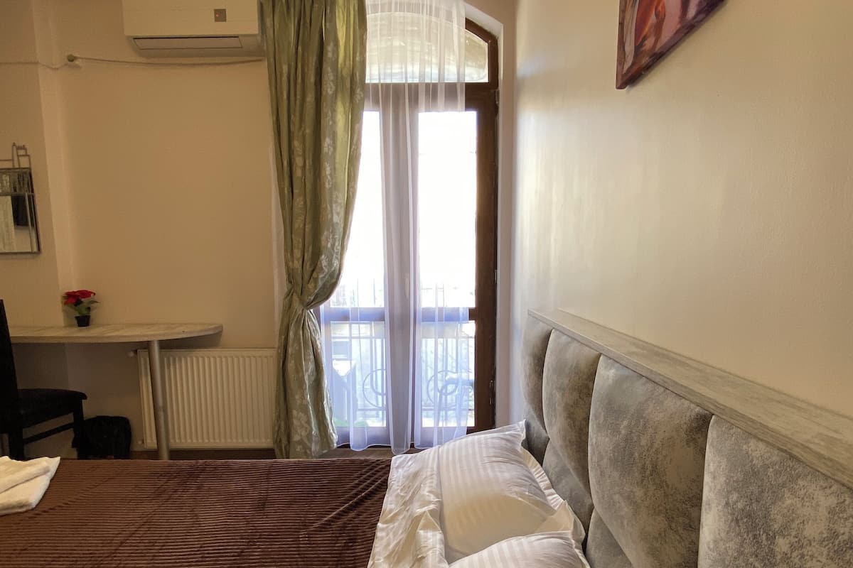 A hotel room with a bed, a desk, a radiator, and a window with curtains.