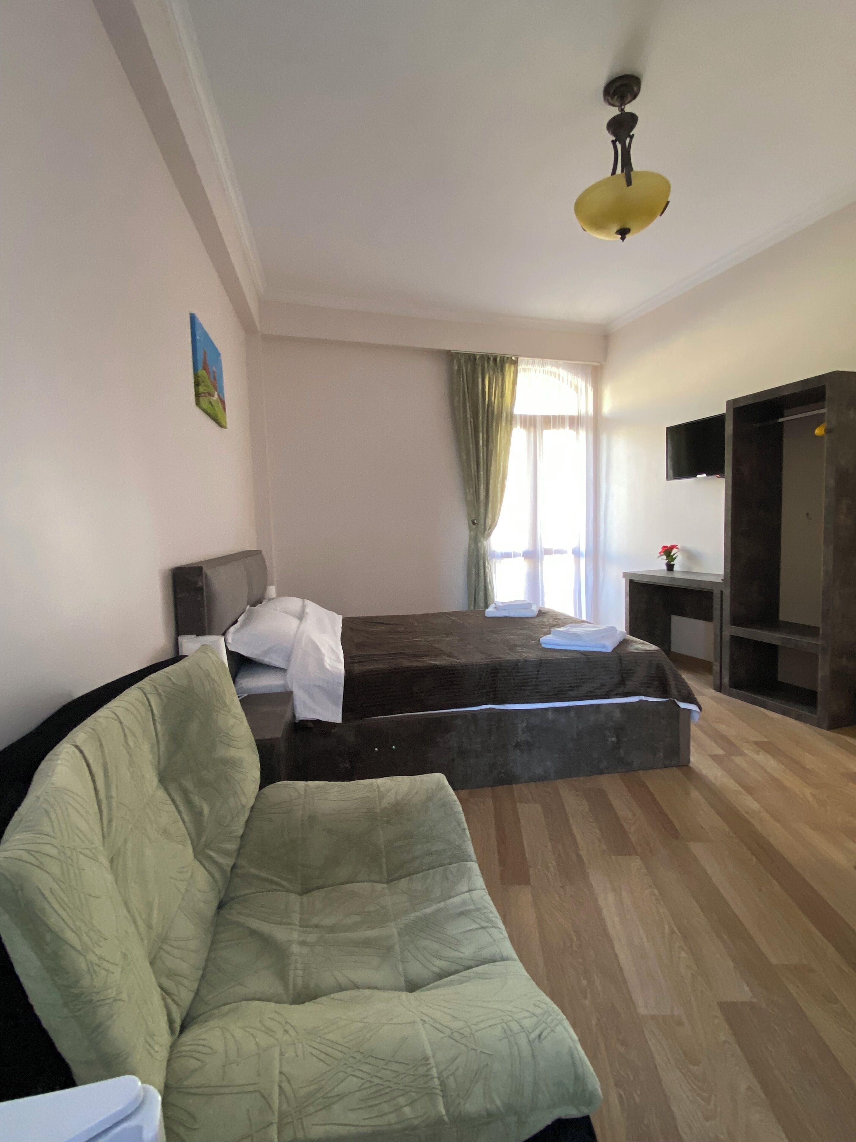 A hotel room with a bed, a sofa, a TV, and a window with curtains.