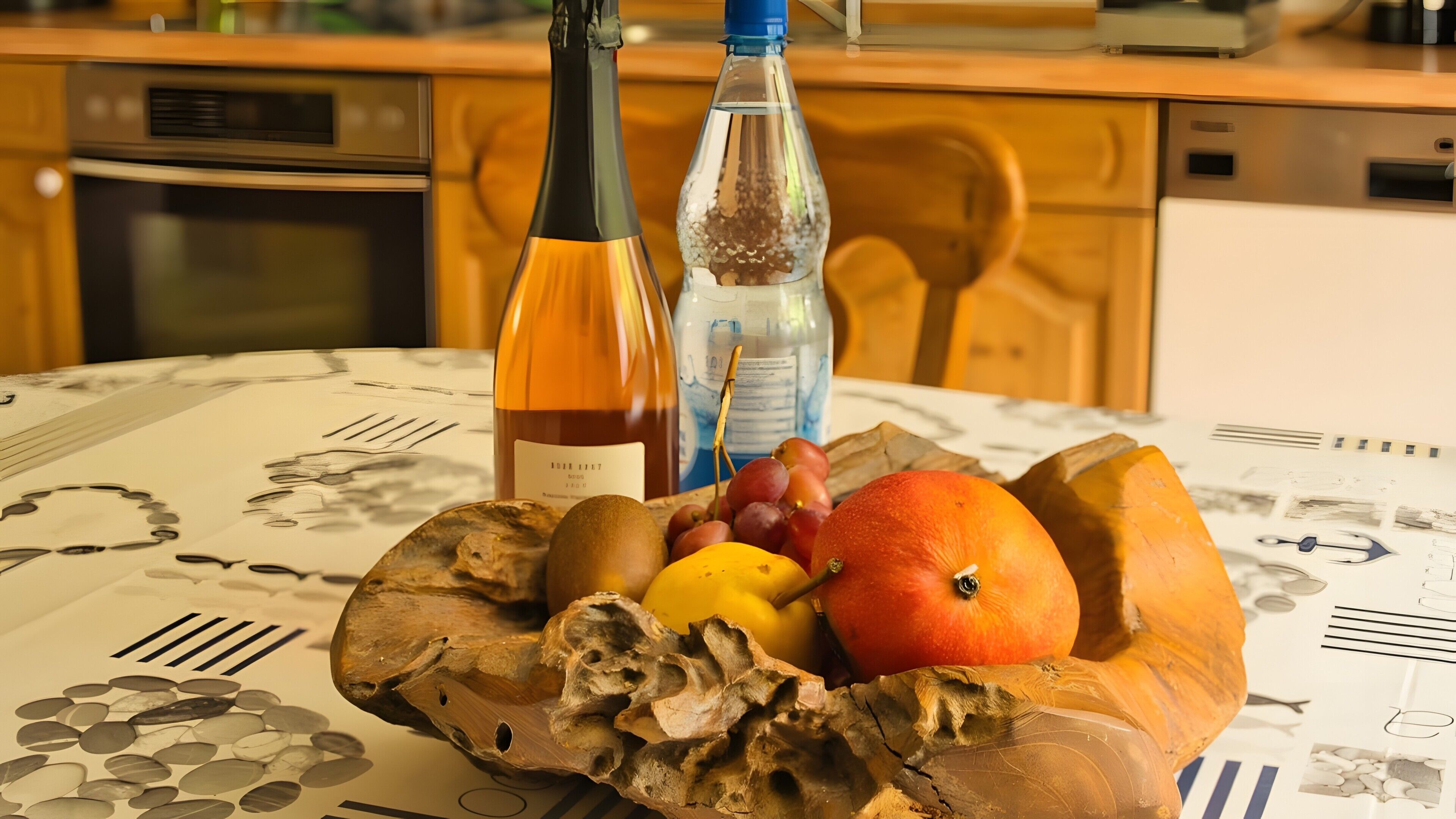 Una mesa con un frutero que contiene uvas, una naranja y una fruta amarilla, una botella de vino y una botella de agua.