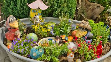 Een tuin met diverse decoratieve elementen, waaronder een tuinbeeldje, een vogelhuisje en kleurrijk beschilderde eieren.