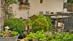 Une terrasse avec des meubles d’extérieur, une plante en pot et un petit espace aménagé en jardin.
