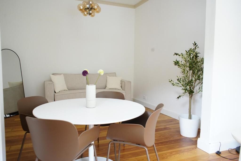 Ein modernes Zimmer mit einem runden weißen Tisch, braunen Stühlen, einem beigen Sofa, einer Zimmerpflanze und einer Stehlampe.