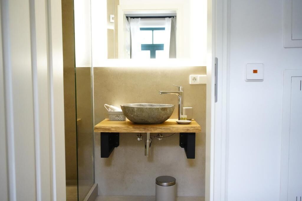 A bathroom with a stone sink, a mirror, and a window with a curtain.