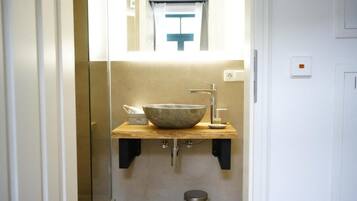 A bathroom with a stone sink, a mirror, and a window with a curtain.