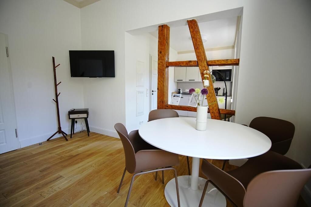A dining area with a round table, brown chairs, a flat-screen TV mounted on the wall, and a wooden beam structure.