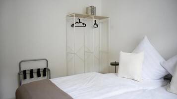 A bedroom with a bed, a white wardrobe, and a metal rack with hangers.