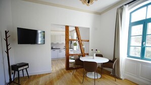 A modern living room with a TV, a dining table with chairs, a wooden structure, and a large window. - Königsgleis-Apartments (Bad Wildbad)