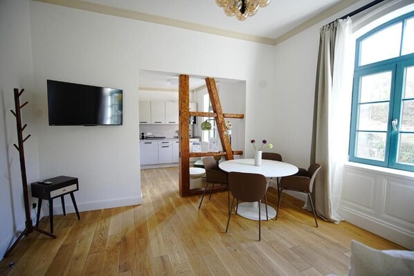 A modern living room with a TV, a dining table with chairs, a wooden structure, and a large window. - Königsgleis-Apartments (Bad Wildbad)