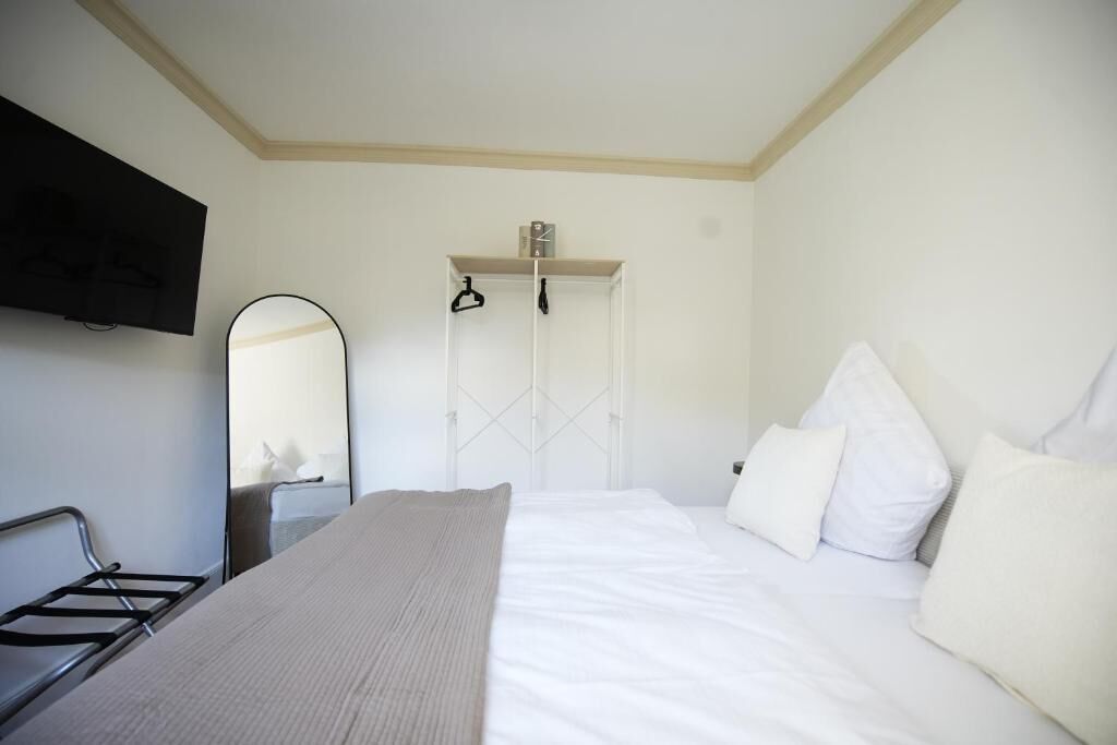 Ein Hotelzimmer mit Bett, Wandfernseher, Spiegel und Schrank mit Uhr.