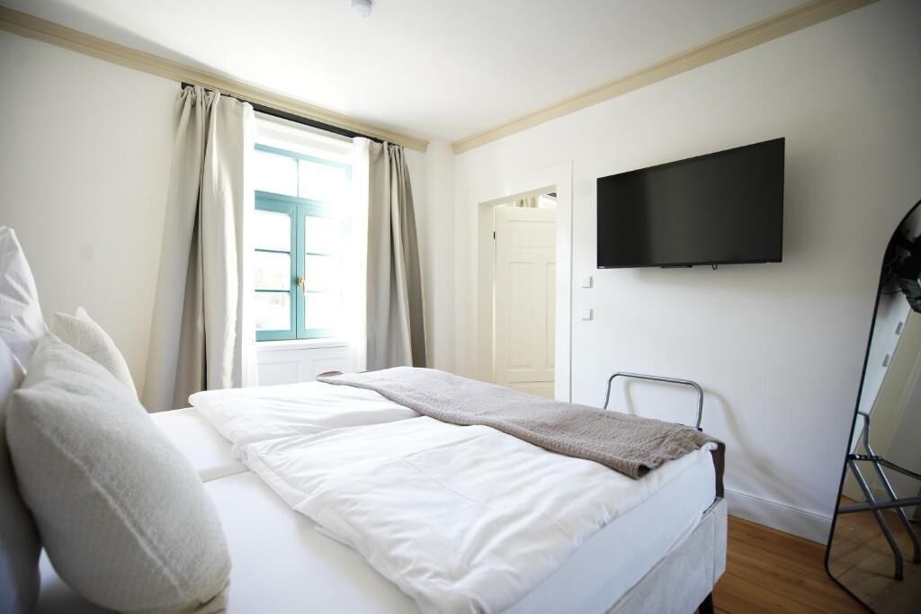 Une chambre d’hôtel avec un lit, un téléviseur fixé au mur et une fenêtre avec des rideaux.