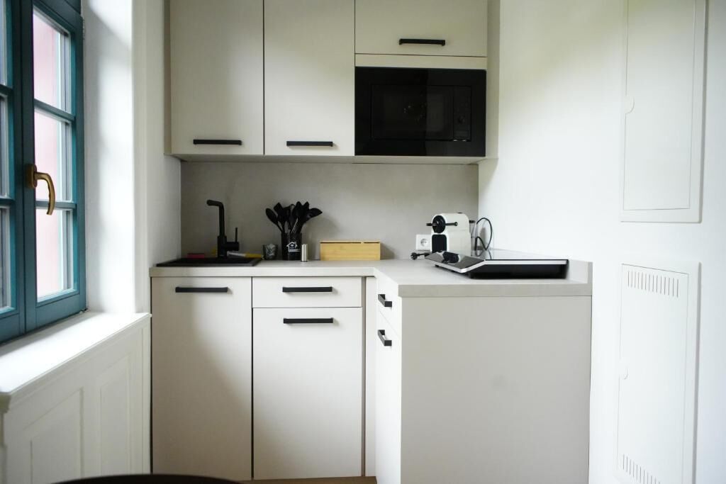 Eine kompakte Küche mit weißen Schränken, einer schwarzen Mikrowelle und einer kleinen Arbeitsplatte mit Toaster und Besteck.