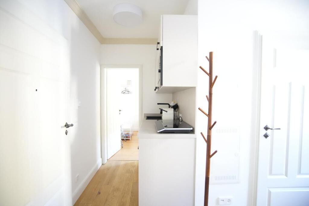 Une cuisine moderne avec des meubles blancs, un plan de travail et une porte visible donnant sur une autre pièce.