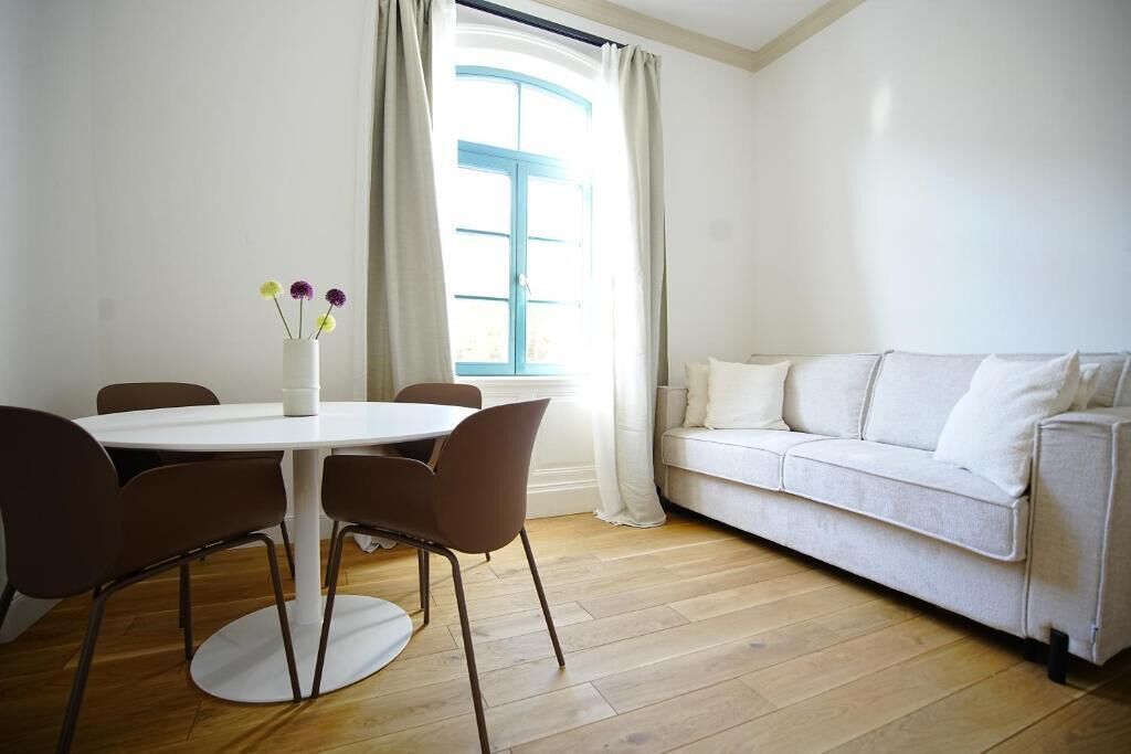 A room with a round table, brown chairs, a white sofa, and a window with curtains.