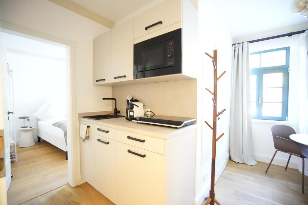 A compact kitchen with a microwave, a coffee machine, and a small dining area with a chair.