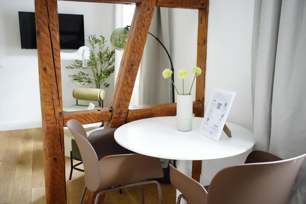 A round white table with a menu, surrounded by four chairs, in a room with wooden beams and a plant.