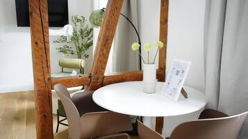 A round white table with a menu, surrounded by four chairs, in a room with wooden beams and a plant.
