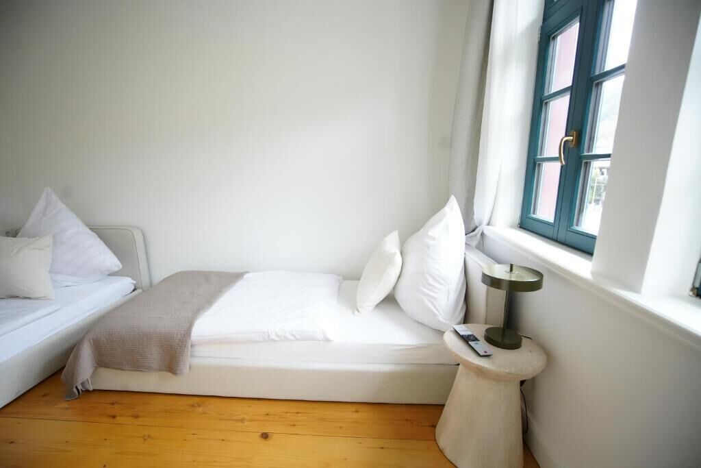 Una stanza piccola e pulita con un letto, un comodino, una lampada e una finestra con tende.