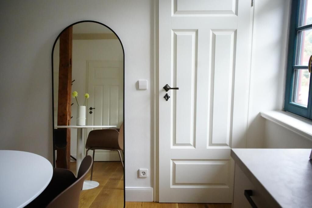 A room with a white door, a mirror, a table, and a chair.