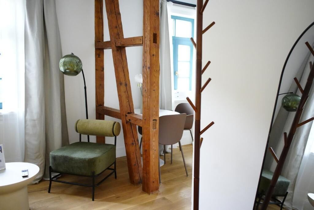 Une pièce dont la structure est constituée de poutres en bois, avec un fauteuil à revêtement vert, une table ronde et un lampadaire.