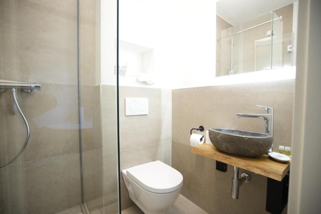 Een moderne badkamer met een glazen douchecabine, een wit toilet en een stenen wastafel met een houten aanrechtblad.