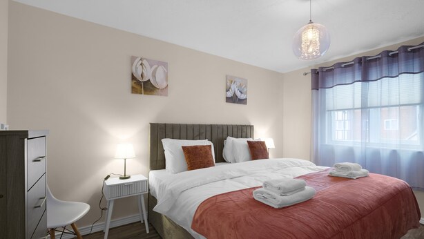 A bedroom with a bed, bedside table, lamp, chair, and artwork on the wall. - Modern 1 Bedroom Apt in Streatham with Parking (London)