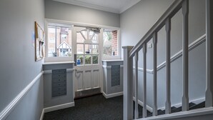 A hallway with a door leading to a window, a staircase, and a wall-mounted cabinet. - Modern 1 Bedroom Apt in Streatham with Parking (London)