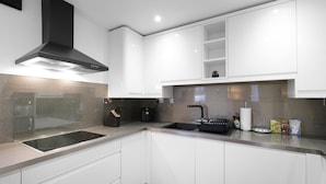 A modern kitchen with white cabinetry, a black range hood, a built-in stovetop, and a stainless steel sink. - Modern 1 Bedroom Apt in Streatham with Parking (London)