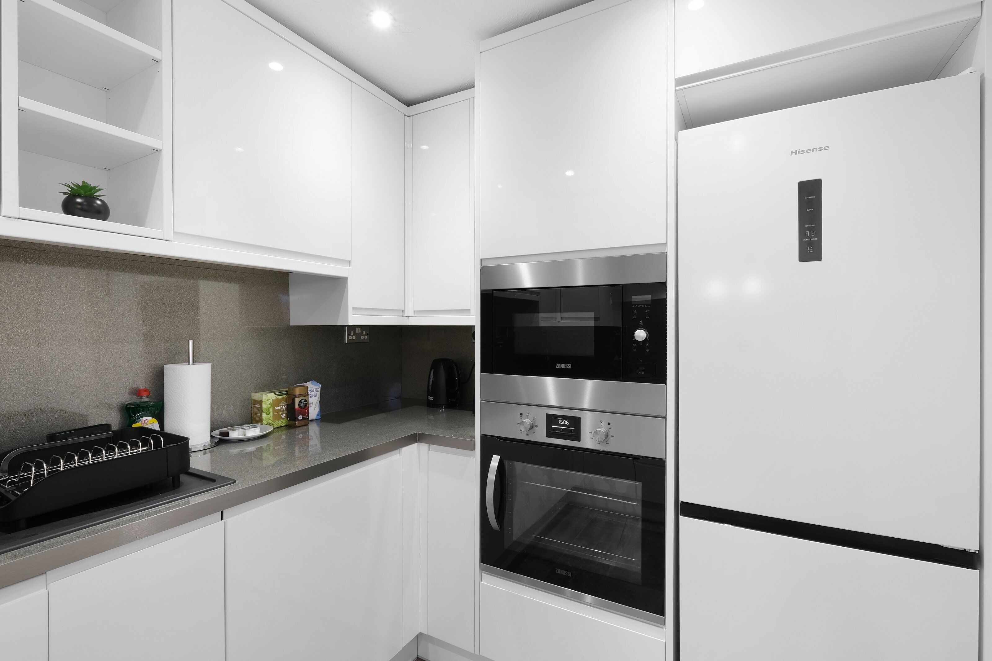 A modern kitchen with white cabinetry, a built-in oven, and a refrigerator.