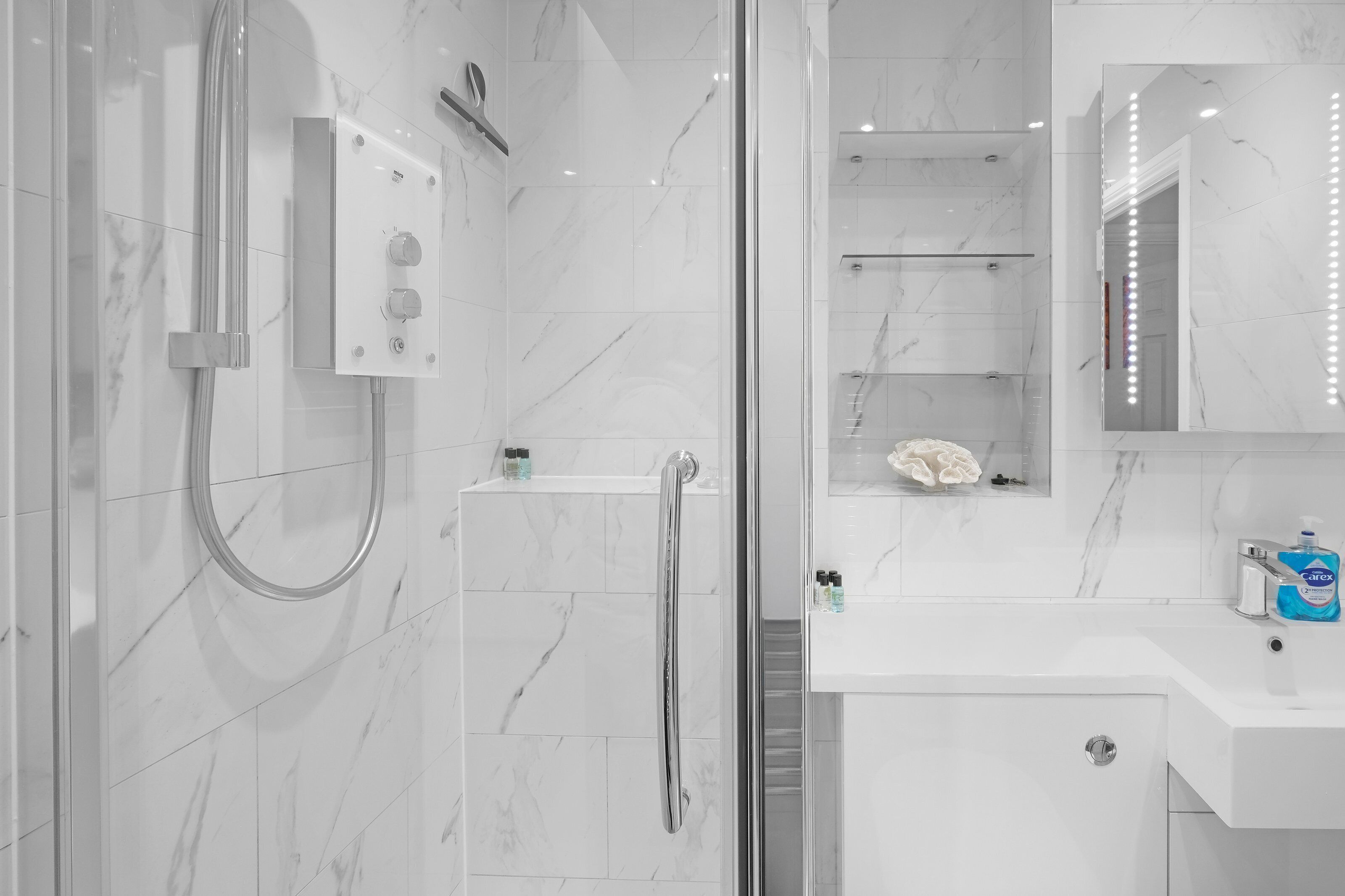 A modern bathroom with a glass-enclosed shower, a vanity with a mirror, and a soap dispenser.