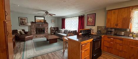 A living room with a fireplace, a sofa, a coffee table, and a kitchen area with cabinets and appliances.