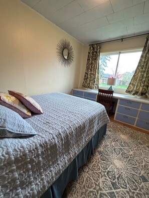A bedroom with a bed, dresser, window with curtains, and a mirror on the wall. - Quiet Meridian Cottage (Boise)