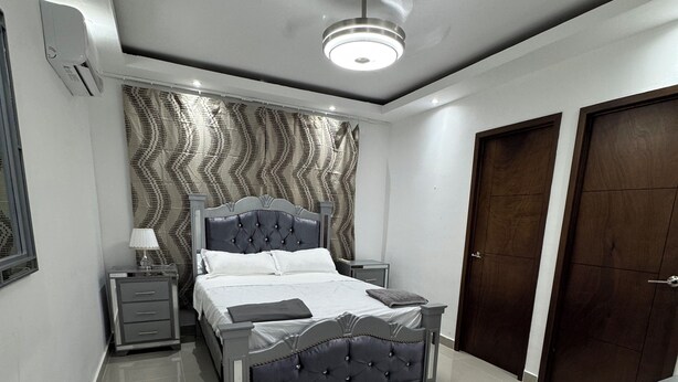 A modern bedroom with a bed, bedside tables, a rug, and a ceiling fan. - Apartment 10 minutes from Las Americas International Airport and the beach. (Santo Domingo Este)