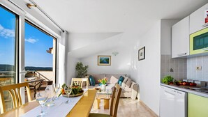 Una cocina moderna con lavavajillas, un comedor con una mesa lista para dos personas y un sofá.
