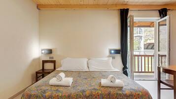 A hotel room with a bed, two bedside tables, a TV, and a balcony with a view.