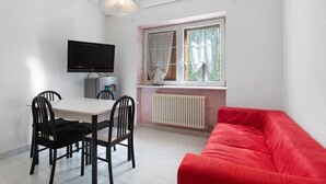 Une pièce comprenant une table à manger, des chaises, un canapé rouge, un téléviseur et une fenêtre avec des rideaux.