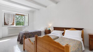 Une chambre à coucher avec deux lits en bois, une fenêtre avec des rideaux, une table de chevet avec une lampe et un radiateur.