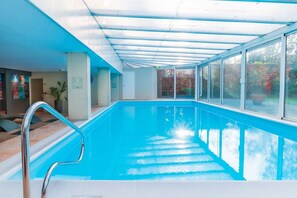 Une piscine intérieure avec des parois en verre transparent, une échelle en métal et un sol carrelé.
