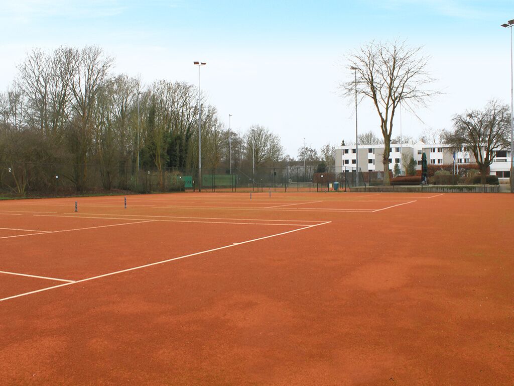 Een buiten tennisbaan met een net, omringd door bomen en gebouwen.