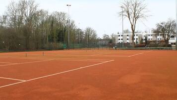 Een buiten tennisbaan met een net, omringd door bomen en gebouwen.