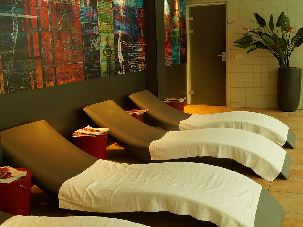 A spa room with reclining chairs, a wall mural, a potted plant, and a tiled wall.