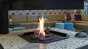 Ein moderner Außenbereich mit Sitzgelegenheiten, einem Feuerkorb, einer Couch und einer Wand mit Muster im Hintergrund.
