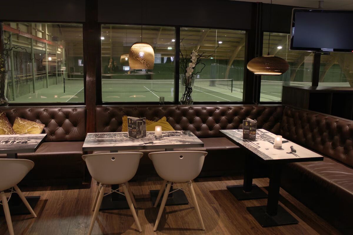 A modern interior with a leather sofa, two white chairs, a table with a candle, and a TV mounted on the wall.