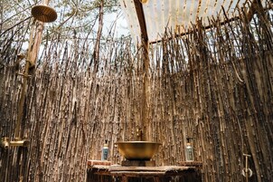 Un ambiente rústico con ducha suspendida, un lavabo de latón y una botella de jabón de baño sobre una plataforma de madera.