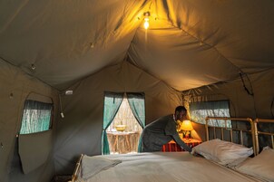 Una carpa con una cama, una mesa con una lámpara y una ventana con cortinas.