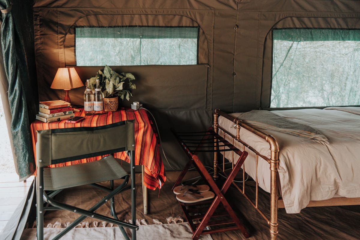 Une tente avec un lit, une table avec des livres et une lampe, et une chaise.