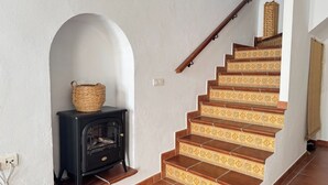 A staircase with patterned steps, a black wood-burning stove, and a woven basket on the wall. - Cozy house in a picturesque white mountain village (Canillas de Albaida)