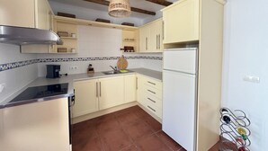 A kitchen with light-colored cabinets, a stainless steel range hood, a white refrigerator, and a hanging light fixture. - Cozy house in a picturesque white mountain village (Canillas de Albaida)
